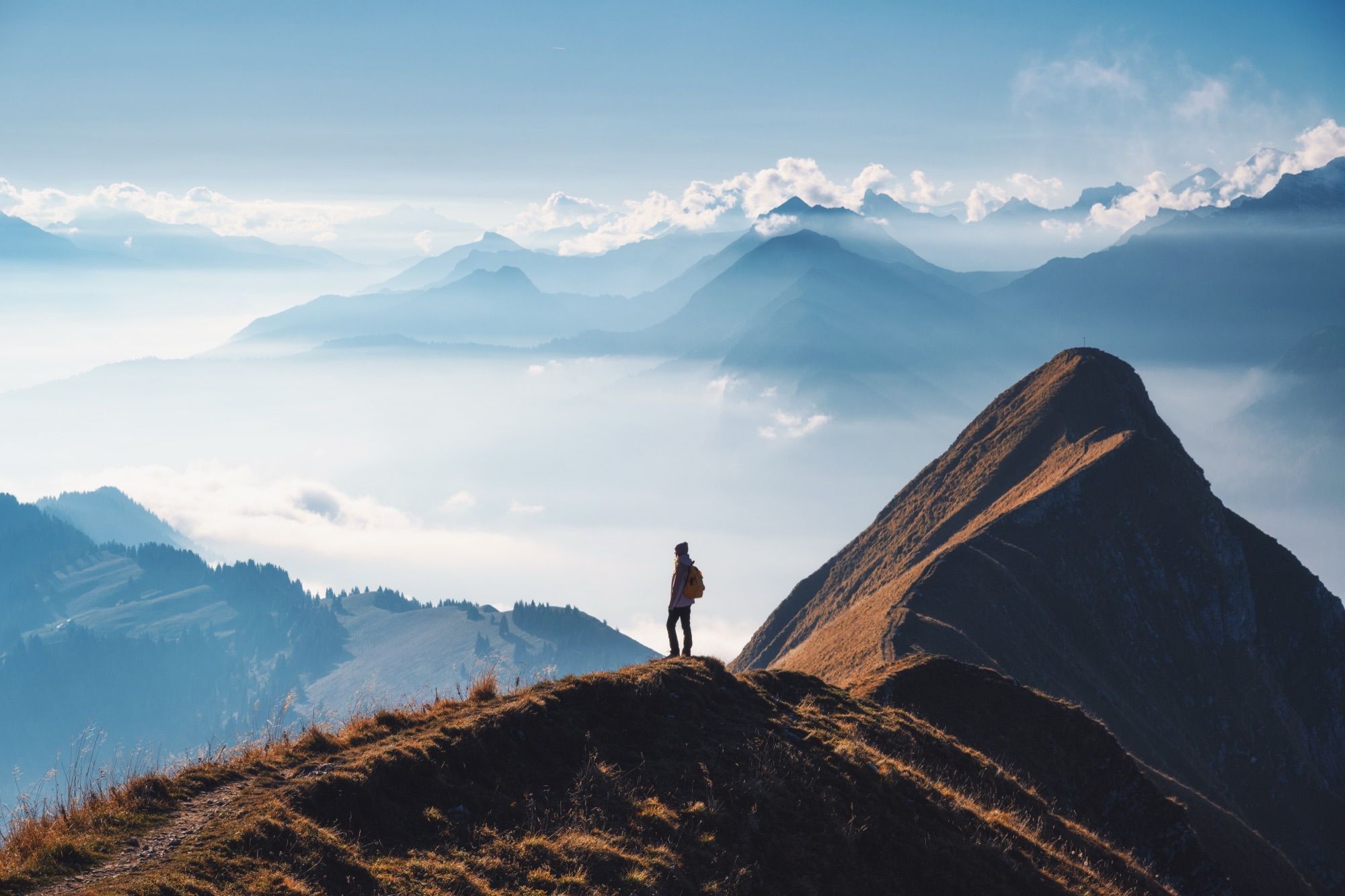 A figure on a mountain ridge overlooking misty peaks